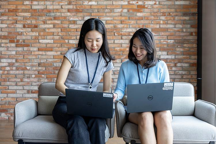 [쿠팡 이미지1] CFDP를 통해 쿠팡에 입사한 구현지 씨(왼쪽)와 조한나 씨가 사내 라운지에서 노트북을 보며 업무에 대해 의견을 나누고 있다.jpg